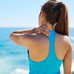 Femme de dos face à la mer avec une douleur d'épaule